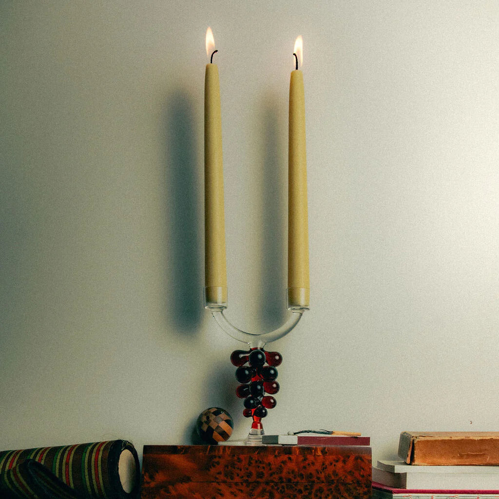Glass candle holder with red grape details. Placed on top of a book with two lit candles