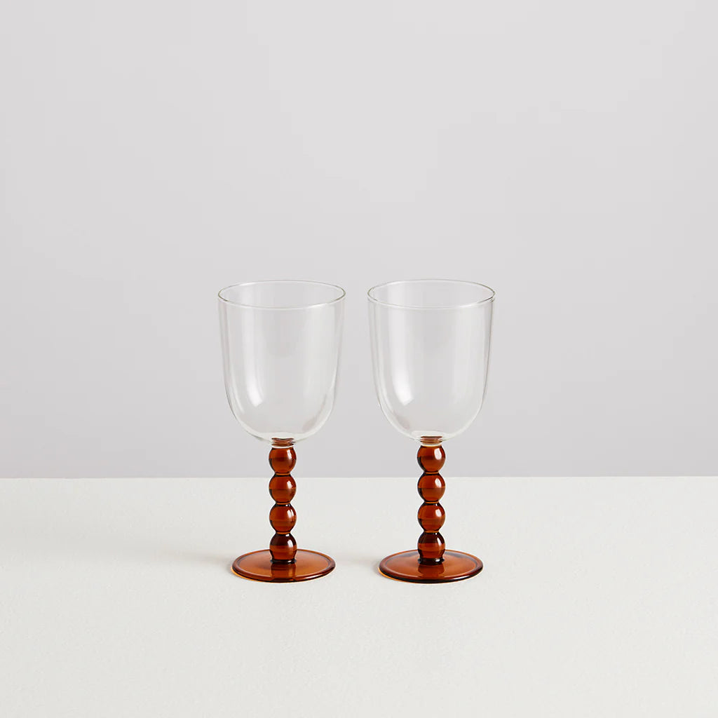 Two wine glasses on a white background. The body of the glasses are clear and the stems and base are formed in amber baubles