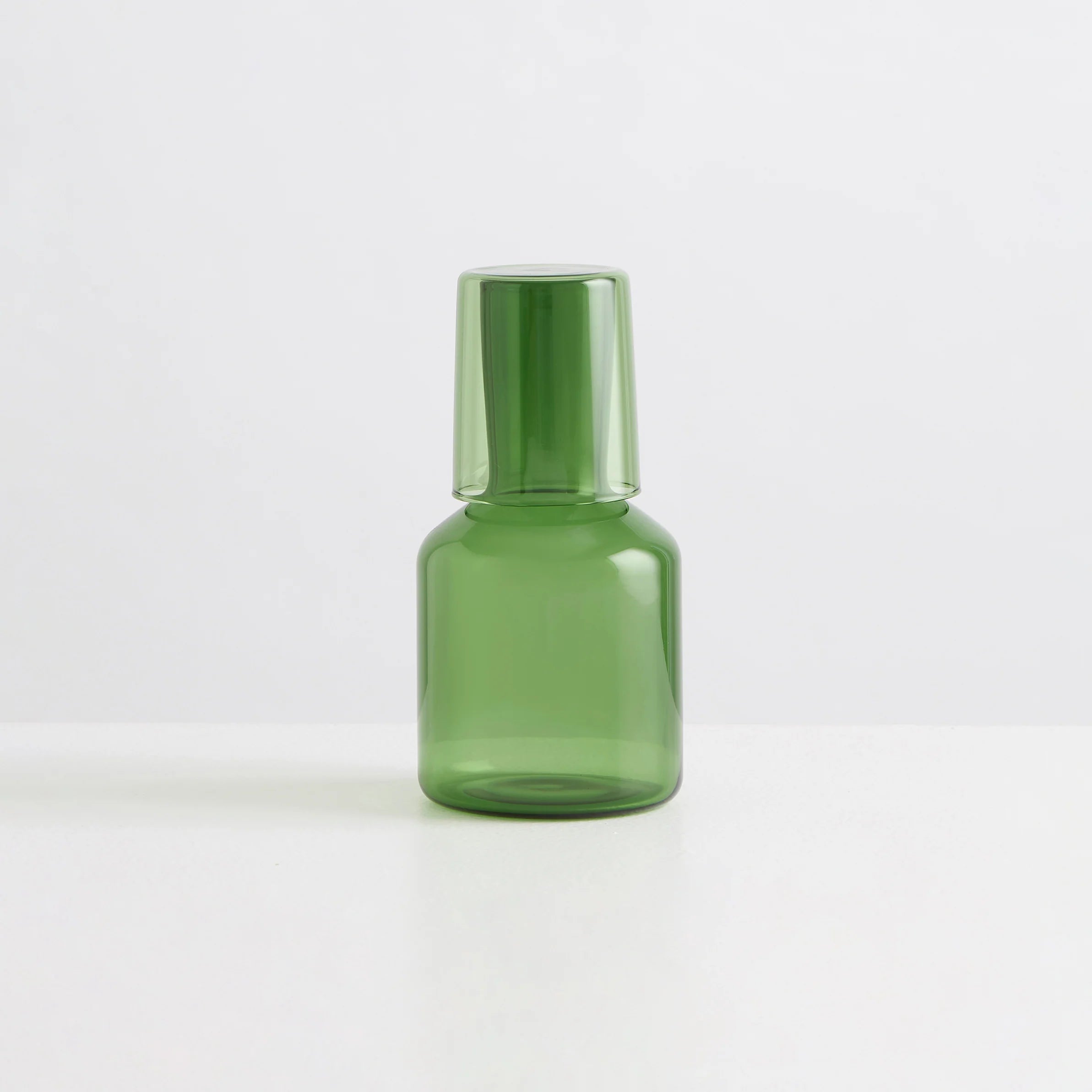 A clear green carafe and drinking glass with the glass on top of the carafe