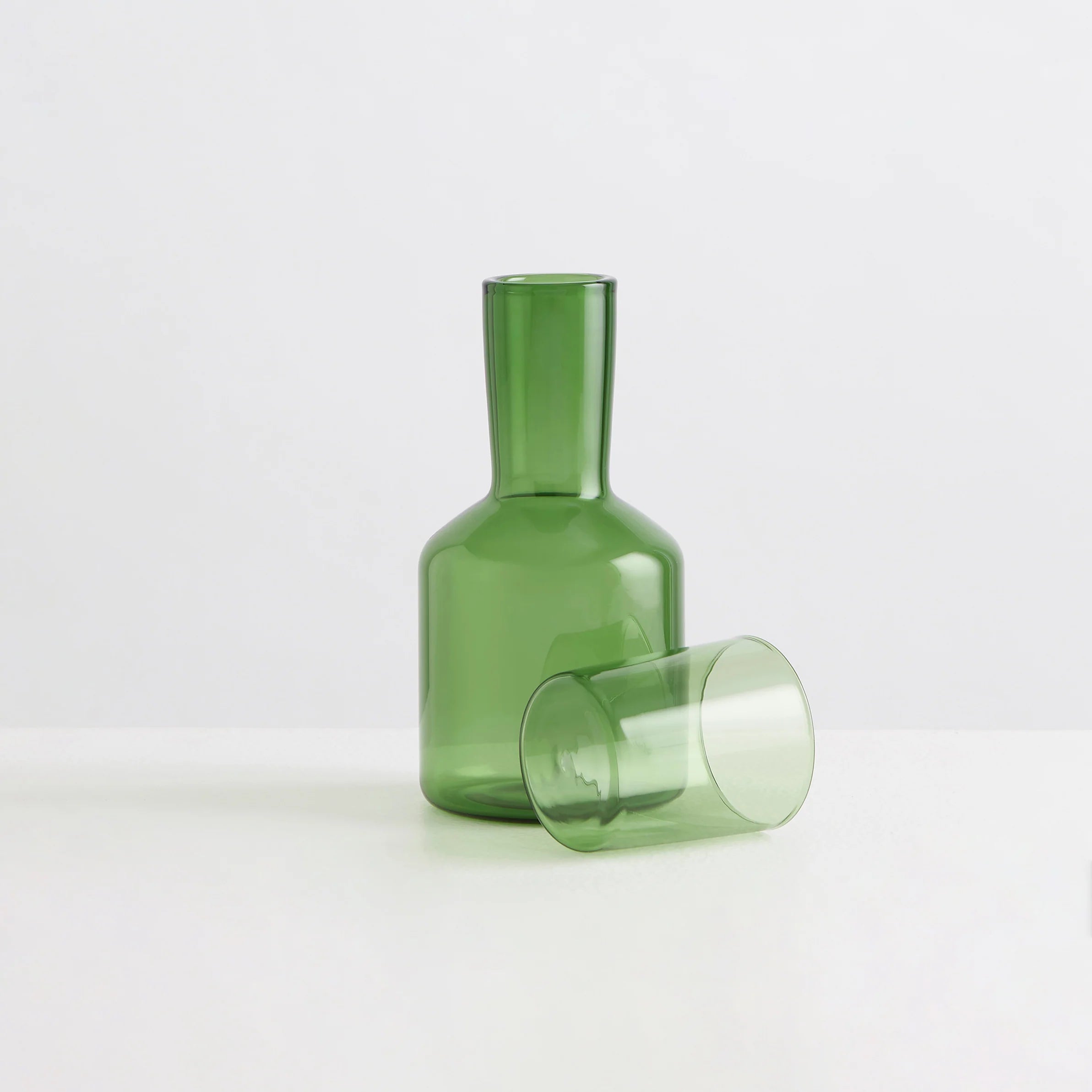 A clear green carafe with a clear green drinking glass lying beside it