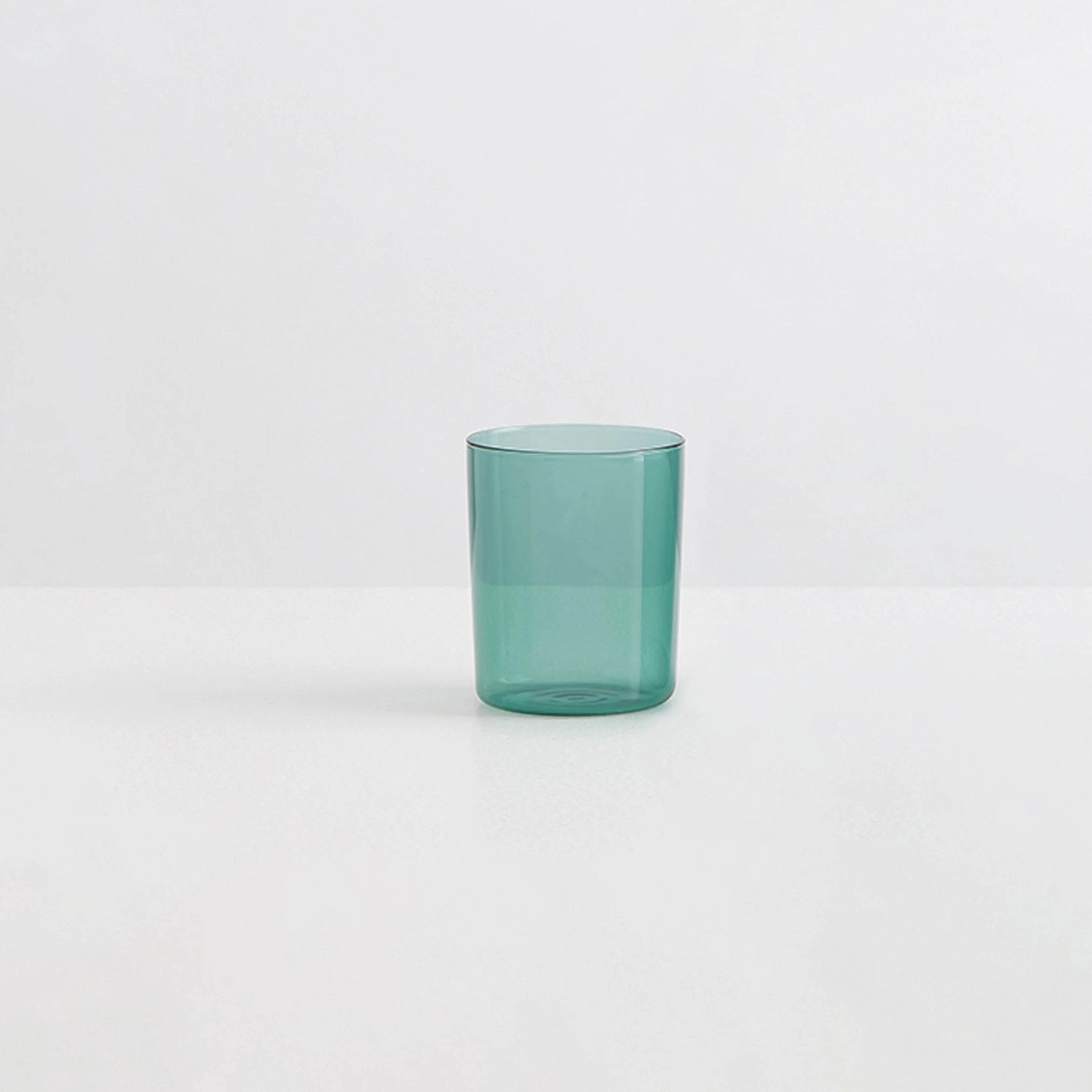A clear teal coloured drinking glass on a white background