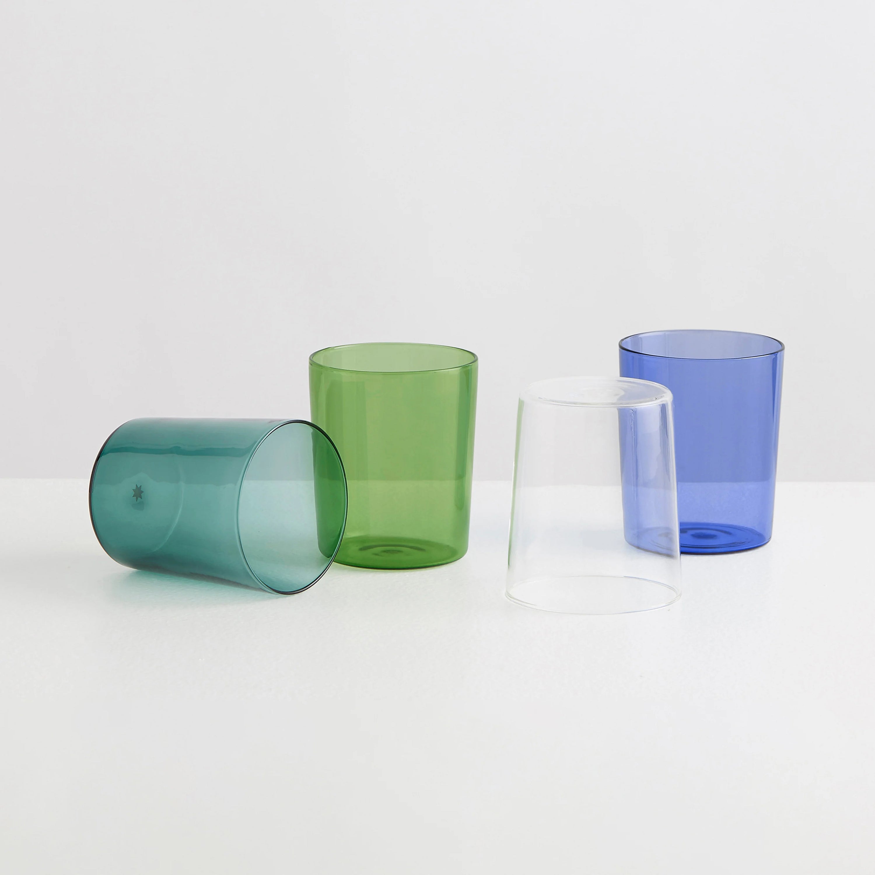 Four clear drinking glasses one teal, one green, one clear and one blue