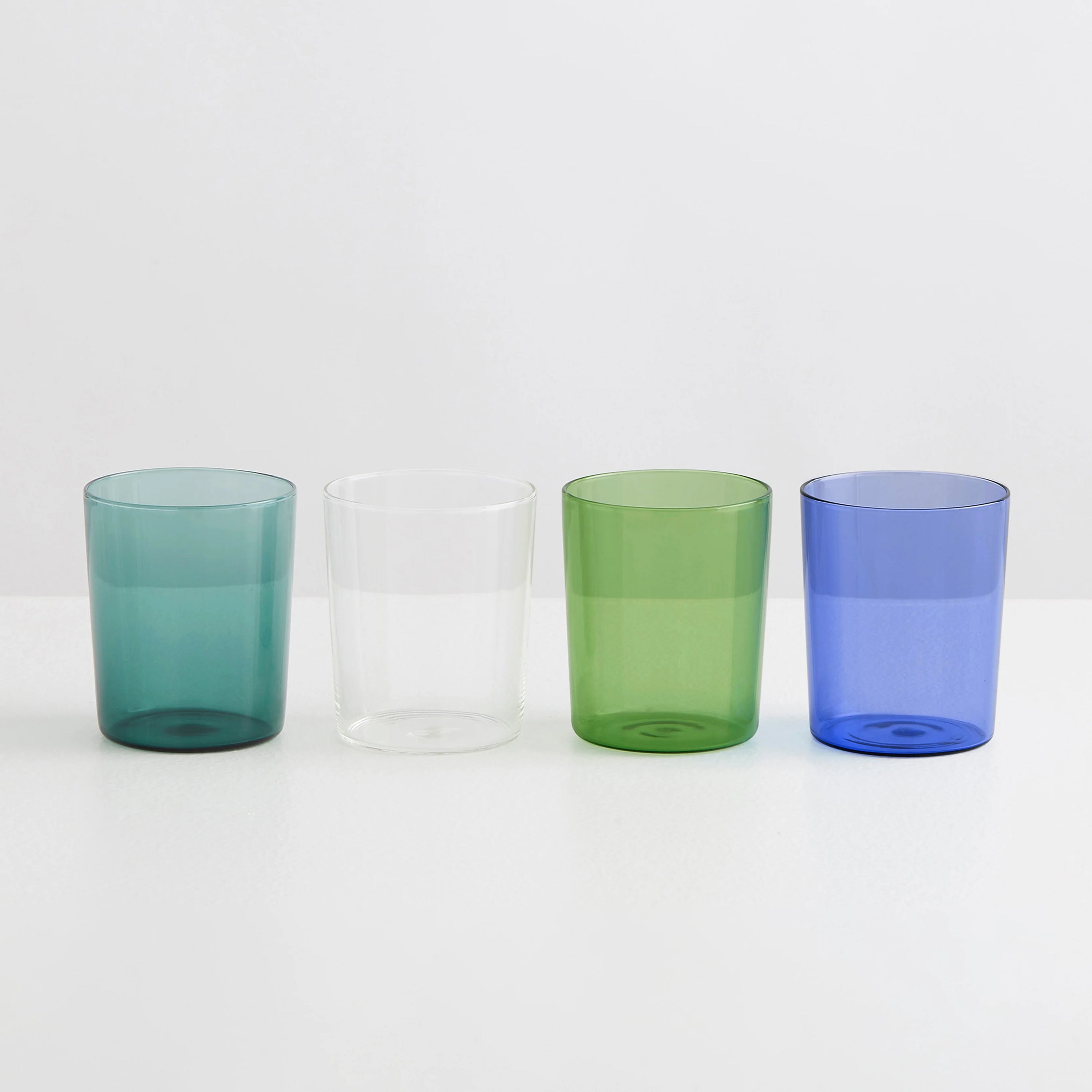 Four clear drinking glasses one teal, one green, one clear and one blue