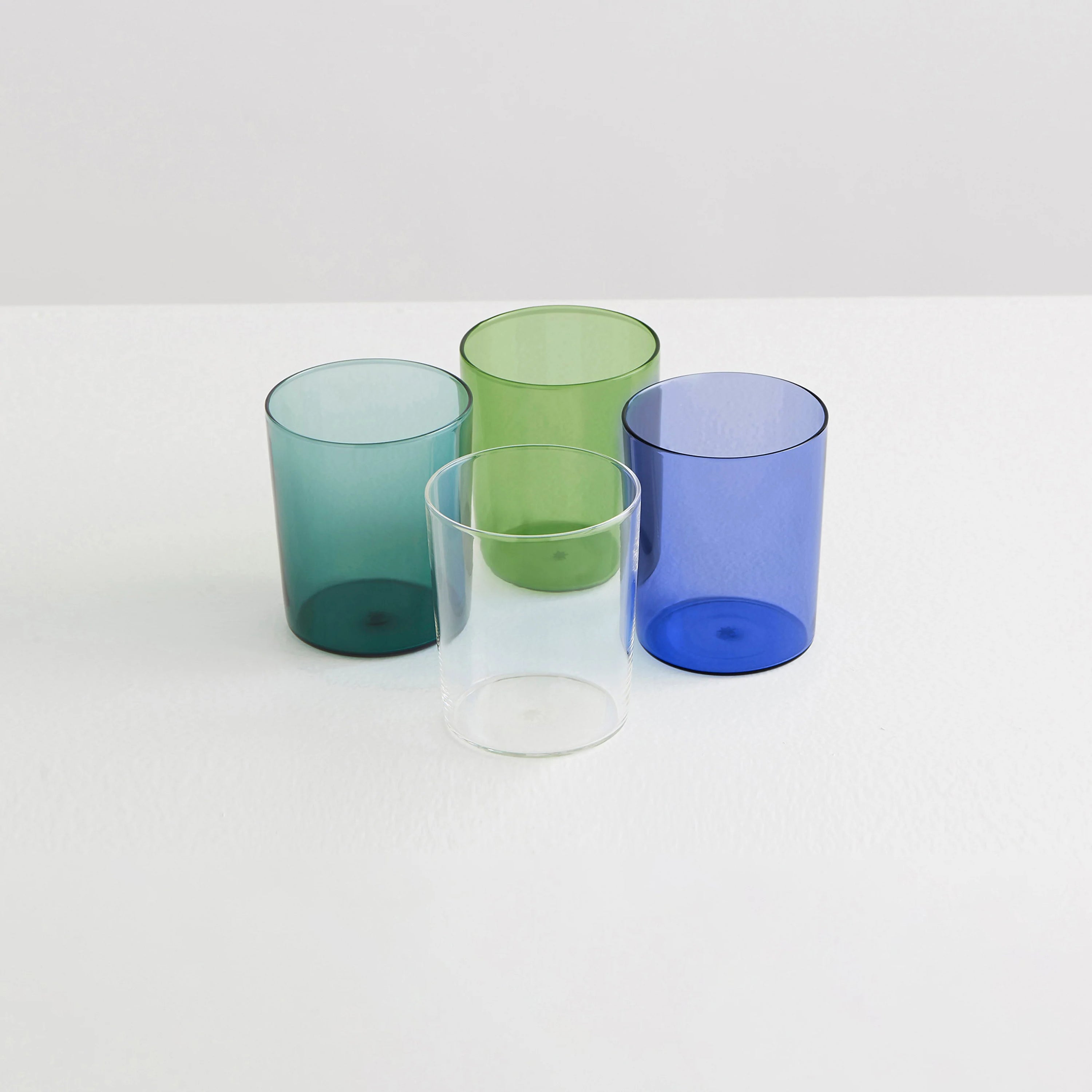 Four clear drinking glasses one teal, one green, one clear and one blue