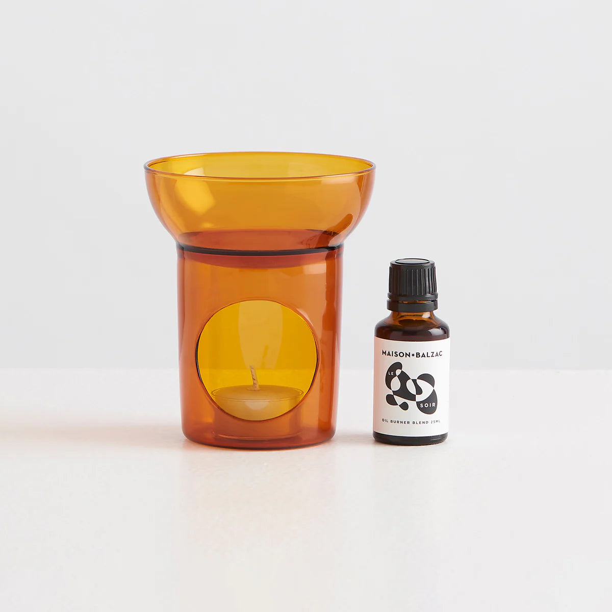 A clear glass amber essential oil burner with a tea light candle sat next to a bottle containing an essential oil blend