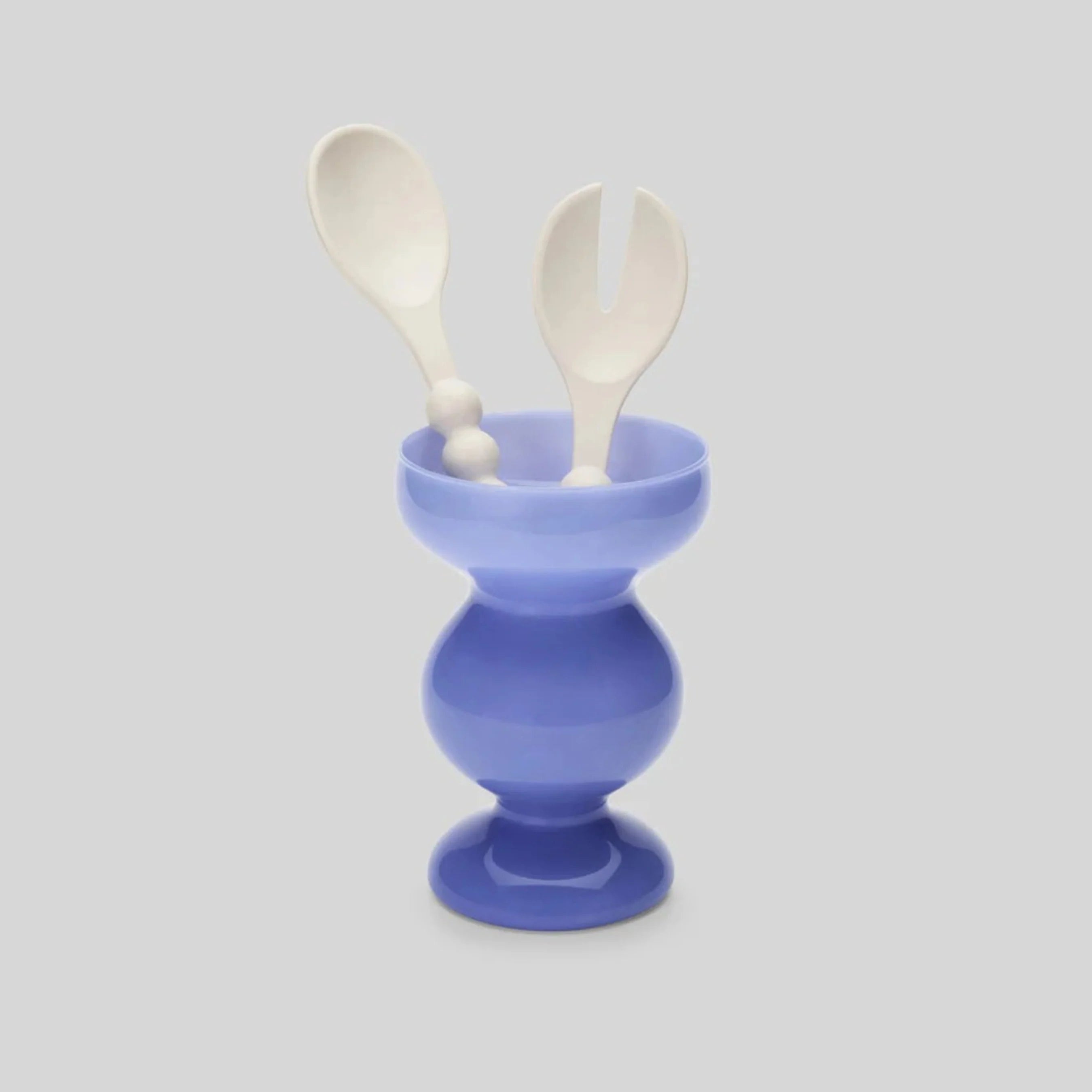 A pale blue glass curvy shaped vase holding a pair of white salad utensils
