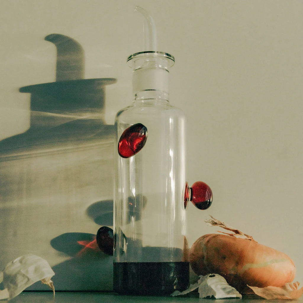 A clear glass bottle with deep red glass olives on it