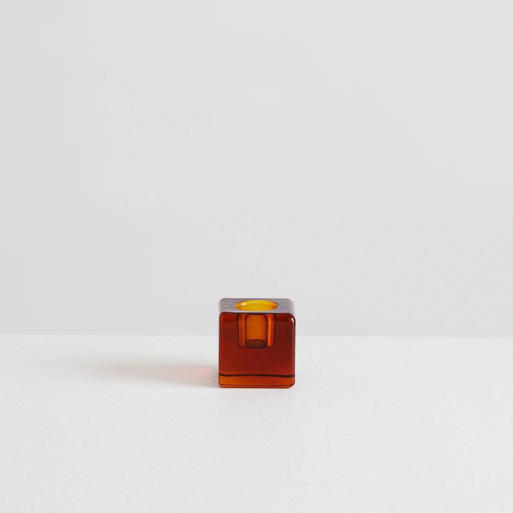 A clear amber glass cube shaped candle holder on a white back ground