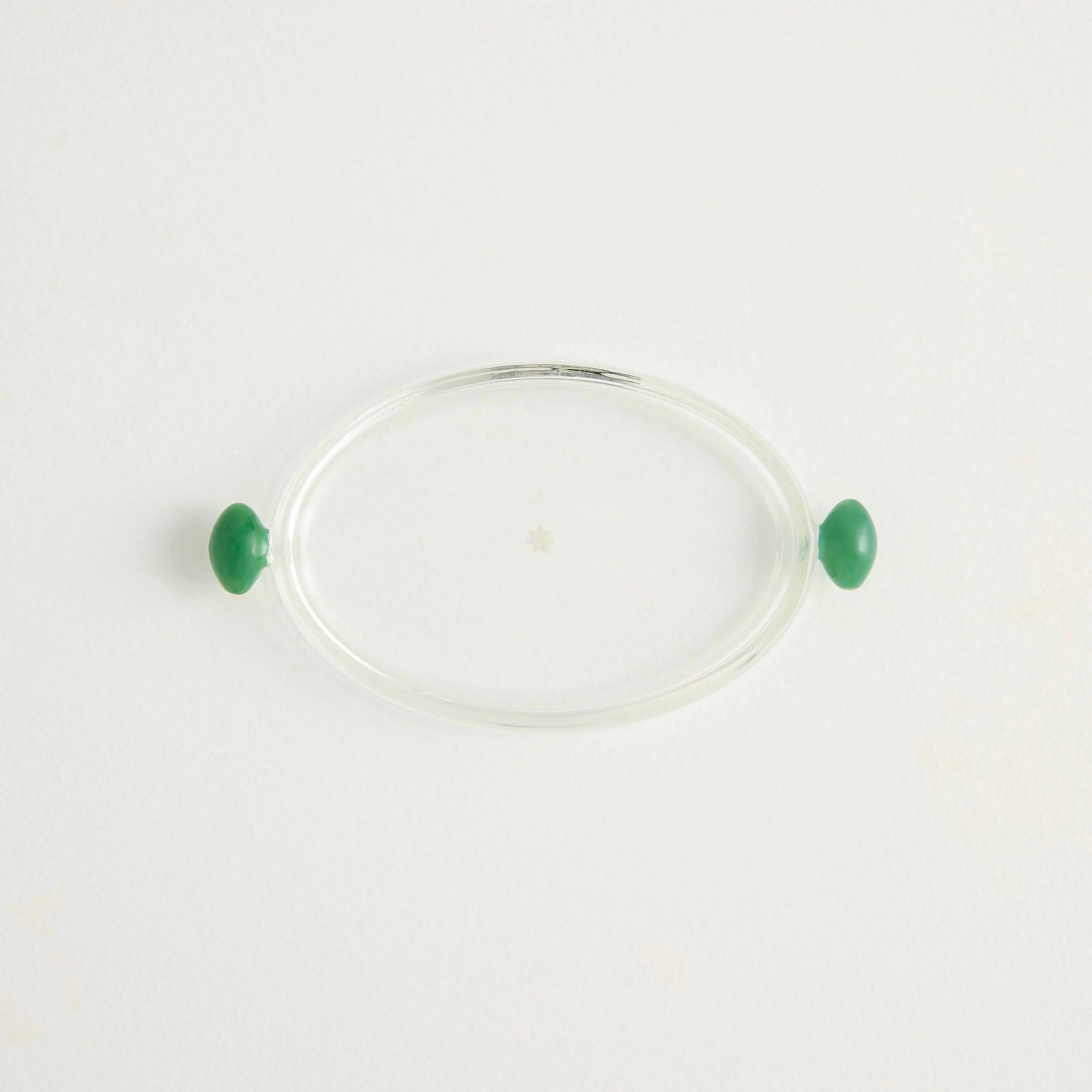 A small glass platter for olives with a glass olive on either side of the clear glass
