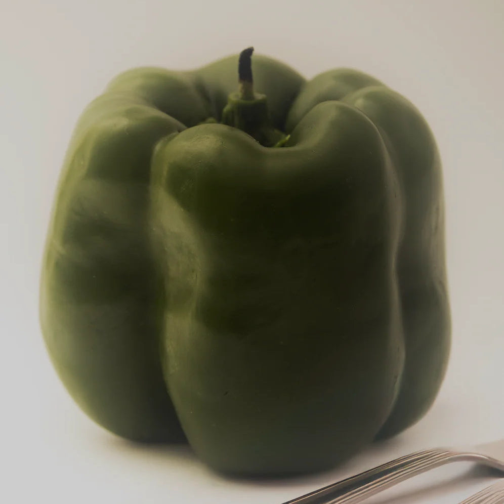 A green capsicum shaped candle on a moody white background